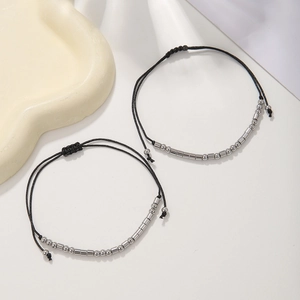 Detail of Morse code bracelets with black woven cord and silver beads on a white surface