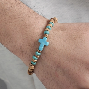 Primer plano de una pulsera para hombre con cruz turquesa y cuentas de madera natural en la muñeca