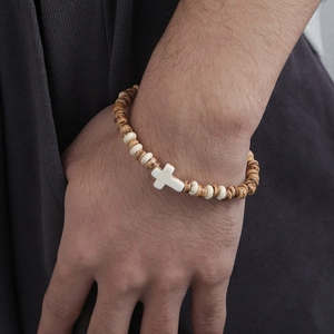 Detalle de pulsera de cuentas de madera con dije de cruz blanca en la muñeca