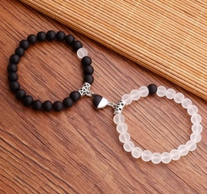 Dettaglio dei braccialetti magnetici per coppia con perle opache nere e bianche su legno