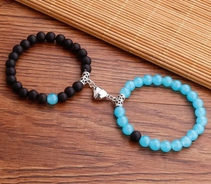 Dettaglio della chiusura magnetica a cuore tra bracciali di perle nere e blu chiaro