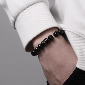 Detalle de la pulsera de cuentas de ónix de 10mm con la letra K dorada en cuenta cuadrada