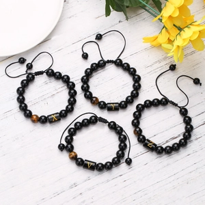 Detalle de pulseras de ónix negro de 10mm con letras doradas y piedras ojo de tigre