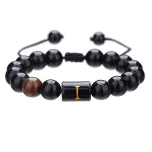 Detalle de pulsera ajustable de ágata negra con la letra I dorada en el centro