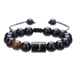 Detalle de pulsera de cuentas de ónix negro de 10mm con cordón trenzado y letra J dorada