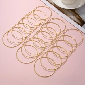 Detailopname van 15 goudkleurige stapelarmbanden met een glinsterende getextureerde finish