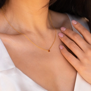 Détail d'un collier minimaliste en or avec pendentif gemme orange sur le cou d'une femme