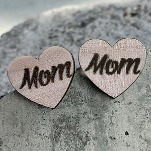 Close-up of heart-shaped rose gold stud earrings with artistic Mom engraving on rock