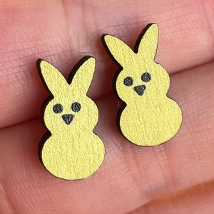 Macro close-up of cute yellow bunny stud earrings held on a finger showing small scale