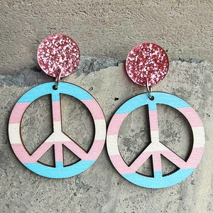 Detail showing peace sign dangle earrings with transgender flag colors and pink sequins