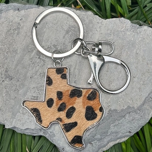 Close-up of leopard print Texas map leather keychain on grey stone and grass background