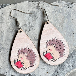 Close-up of teardrop wooden earrings with cute hedgehog reading a book illustration