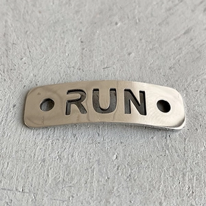 Macro detail of silver cutout metal shoelace charm featuring RUN lettering and side holes