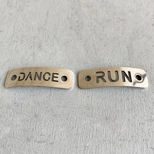 Macro view of silver metal shoe charms featuring hollow DANCE and RUN lettering details