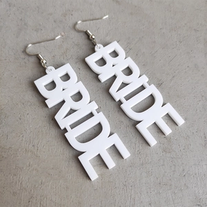 Detailaufnahme der weißen Acryl BRIDE Buchstaben Ohrringe mit Metallhaken auf grau