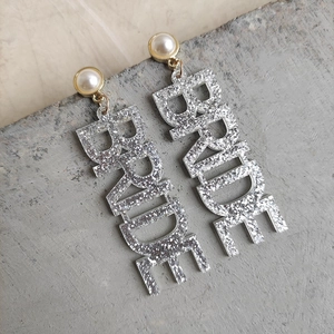 Detail von Perlenohrringen mit silber glänzendem BRIDE-Schriftzug für Hochzeiten