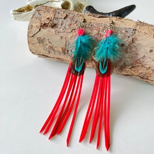 Detail of red tassel earrings with peacock feathers and copper hooks on wood