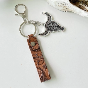 Close-up of western leather keychain with embossed pattern and rhinestone cow head pendant