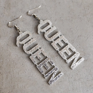 Gros plan sur les boucles d'oreilles QUEEN en acrylique à paillettes argentées sur gris
