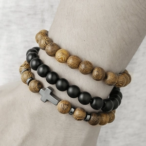 Detailed view of three stacked men's bracelets with wooden beads and a hematite cross charm