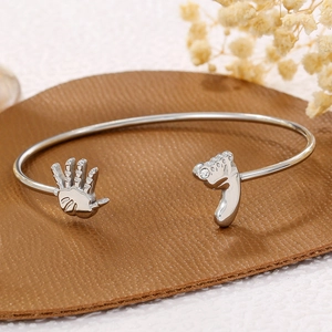 Detail of silver baby hand and footprint bangle with zircon inlay on leather backdrop