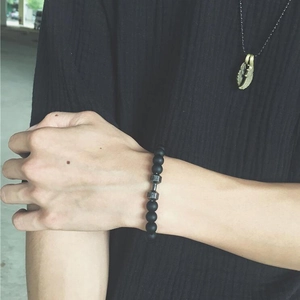 Gros plan d'un bracelet en perles noires mates et collier plume dorée sur un mannequin