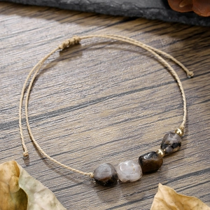 Dettaglio del bracciale artigianale in corda intrecciata beige con pietre naturali grezze