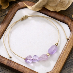 Dettaglio del bracciale intrecciato a mano con pietre grezze viola e perline d'oro su vassoio