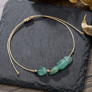 Dettaglio di bracciale intrecciato a mano con pietre grezze verdi e perline dorate