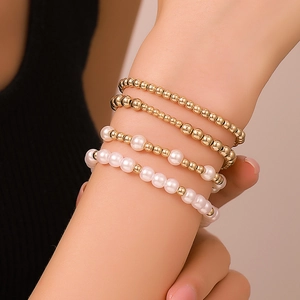 Dettaglio di un set di braccialetti elastici con perline dorate e perle bianche