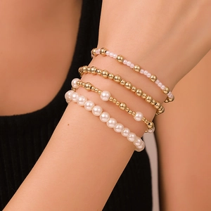 Dettaglio di un set di braccialetti con perline oro e bianche indossati al polso