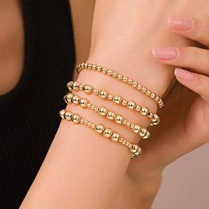 Dettaglio ravvicinato di set di bracciali a sfere dorate lucide indossati sul polso