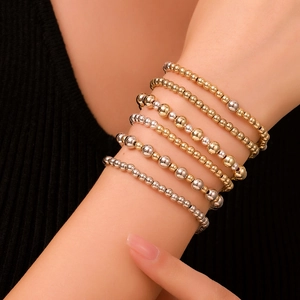 Primo piano di braccialetti impilabili in oro e argento con perline sul polso di un modello