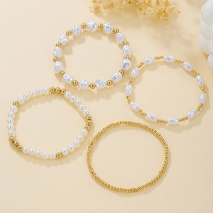 Dettaglio di quattro bracciali con perle irregolari e sfere dorate su sfondo beige caldo