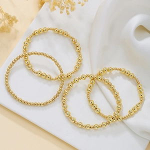 Dettaglio di un set di 4 braccialetti con perline dorate con croce e perle su seta bianca
