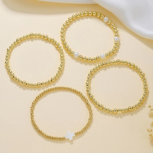 Dettaglio di un set da 4 braccialetti elastici con perline dorate e ciondolo a croce