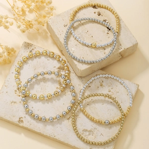 Dettaglio di set braccialetti con perline oro e argento su sfondo di pietra minimalista.