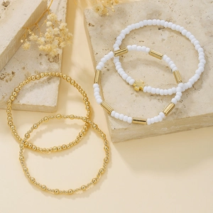 Dettaglio di un set di 4 braccialetti con perline oro e bianche e ciondolo a croce piccolo