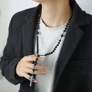 Men's long beaded necklace with a black stone cross pendant worn on a grey suit jacket