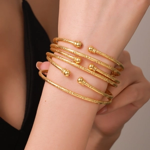 Detailopname van diverse getextureerde vergulde open armbanden met ronde kralen om pols