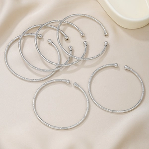 Set van zeven zilveren open armbanden met matte textuur en kraaluiteinden op satijn