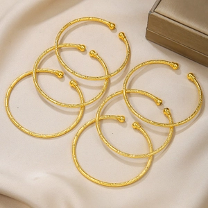 Detailweergave van 6 vergulde open armbanden met geweven textuur op beige zijden stof