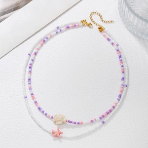 Detail of layered beaded necklace with starfish and turtle charms on a white surface