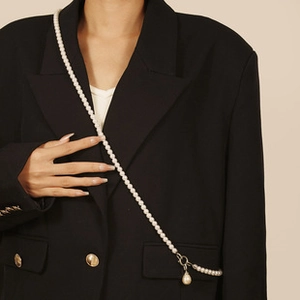 Detailed view of an elegant long pearl crossbody necklace on a black blazer jacket