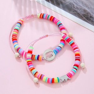 Dettaglio di bracciali colorati in perline Heishi con ciondoli a orso e cordino rosa intrecciato
