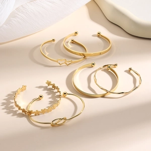 6-delige gouden armbandenset met hart-, knoop-, bloem- en LOVE-motieven op beige achtergrond