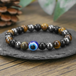 Detailaufnahme von Tigerauge- und Lavasteinperlen mit blauem Evil Eye auf Steintablett