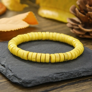 Detalle de pulsera de cuentas de madera amarillas con cordón elástico en bandeja de pizarra