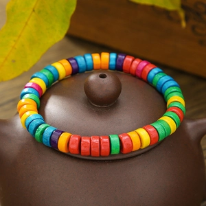 Pulsera elástica de cuentas de madera arcoíris sobre tapa de tetera con hojas de otoño