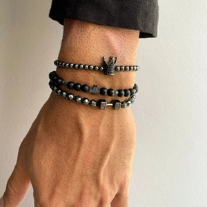 Close-up of men's beaded bracelet set featuring crown, cross, and dumbbell charms